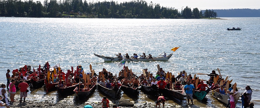 People enjoying a canoe journey landing on a beautiful day at Tulalip Bay